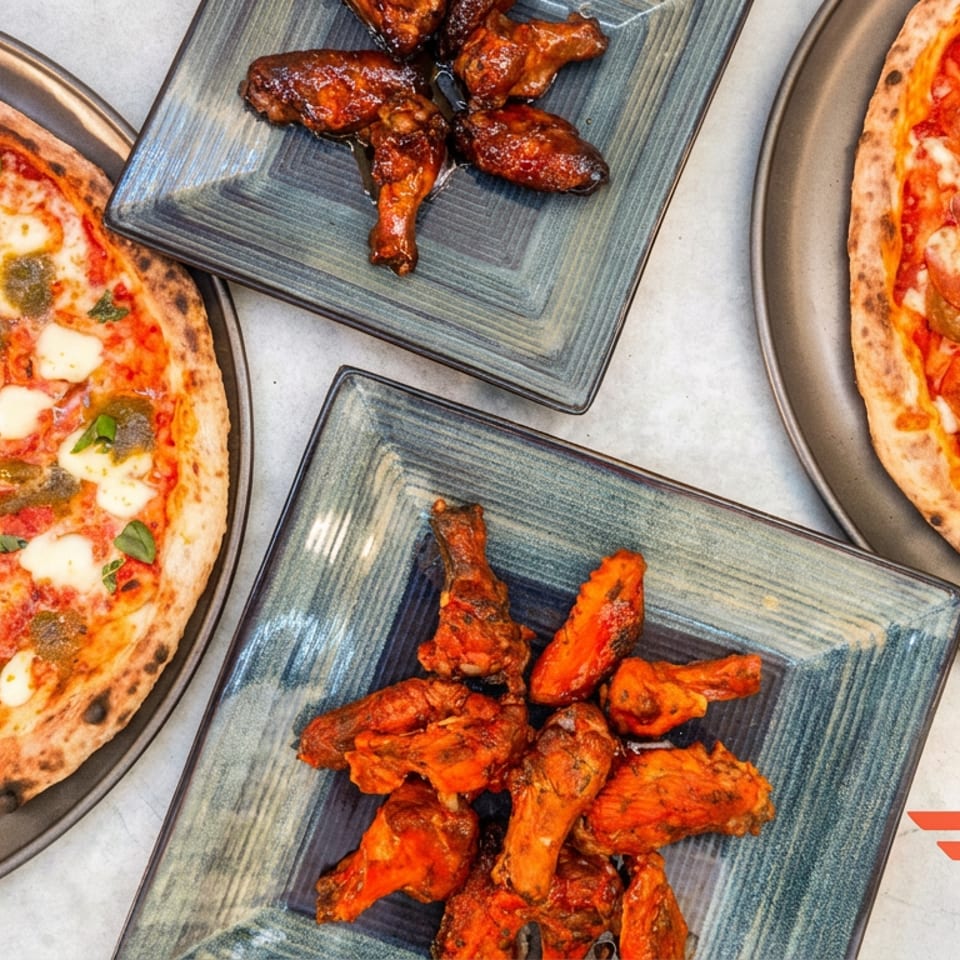 Overhead spread of two pizzas and two plates of saucy chicken wings on a tabletop, with a DoorDash logo.